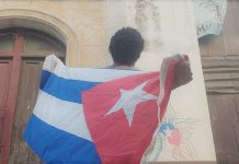 El artista Luis Manuel Otero Alcántara sostiene una bandera cubana frente a una cámara de vigilancia policial
