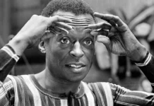 Miles Davis: un poliedro musical y humano Retrato en blanco y negro del trompetista Miles Davis enmarcando su rostro con ambas manos y mirada intensa, en un estudio de grabación.