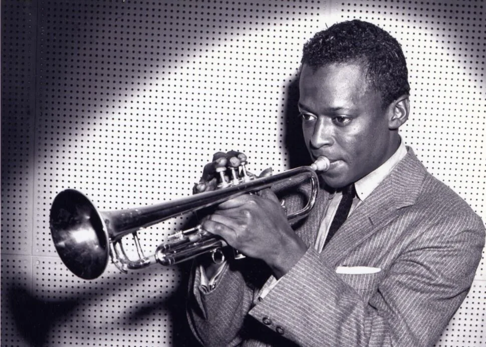 Miles Davis joven, de saco y corbata, tocando la trompeta. Fotografía en blanco y negro, hacia 1953.