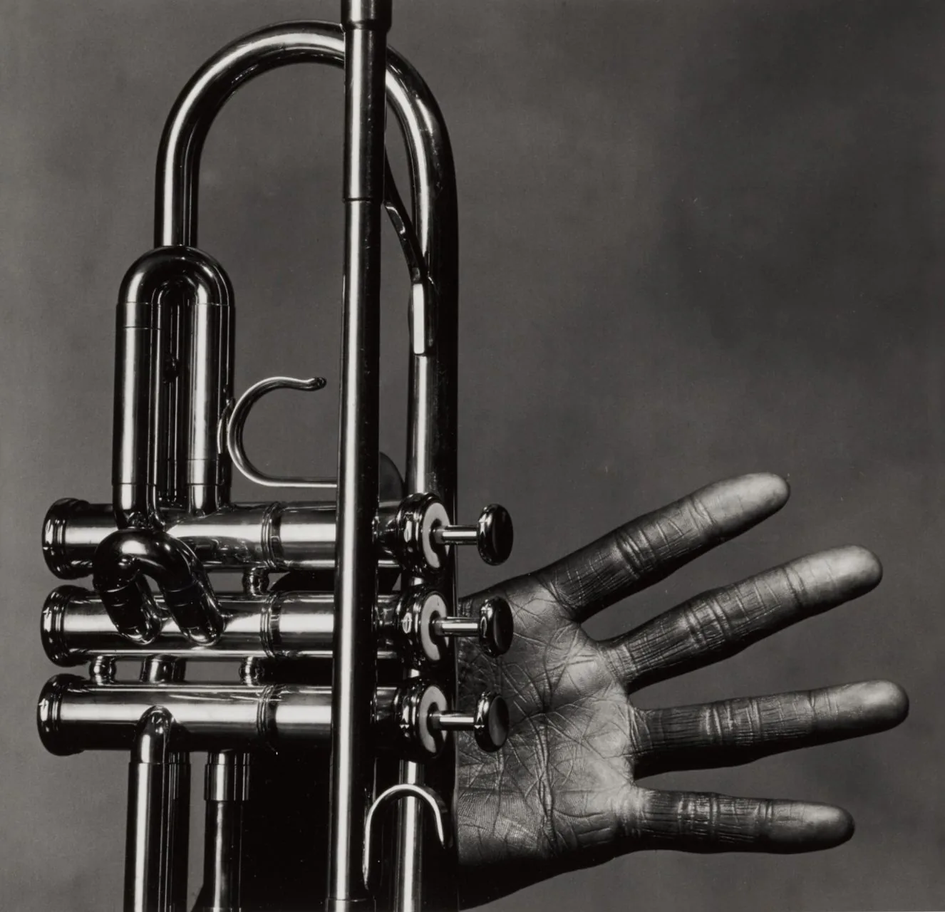 Primer plano en blanco y negro de la trompeta y la mano abierta de Miles Davis, con la palma hacia la cámara, fotografiada por Irving Penn.