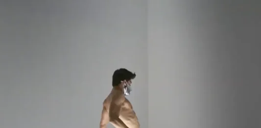 un bailarín con slip plateado y mascarilla sobre la plataforma iluminada de ‘Untitled’ (Go-Go Dancing Platform) de Félix González-Torres.