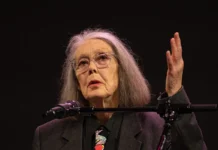 La poeta canadiense Anne Carson conquista el Premio Nobel de Literatura 2026 Anne Carson, de cabello gris y gafas, habla desde un atril con micrófono durante un acto cultural.
