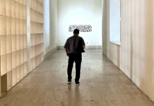 Flavio, creyente Flavio Garciandía, de espaldas, camina por el pasillo de entrada del MARCO de Monterrey hacia el rótulo de su retrospectiva Autorretrato no autorizado