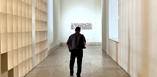 Flavio Garciandía, de espaldas, camina por el pasillo de entrada del MARCO de Monterrey hacia el rótulo de su retrospectiva Autorretrato no autorizado