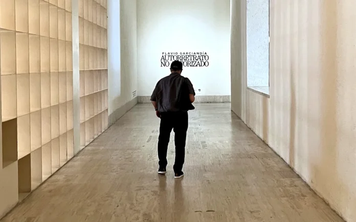 Flavio Garciandía, de espaldas, camina por el pasillo de entrada del MARCO de Monterrey hacia el rótulo de su retrospectiva Autorretrato no autorizado
