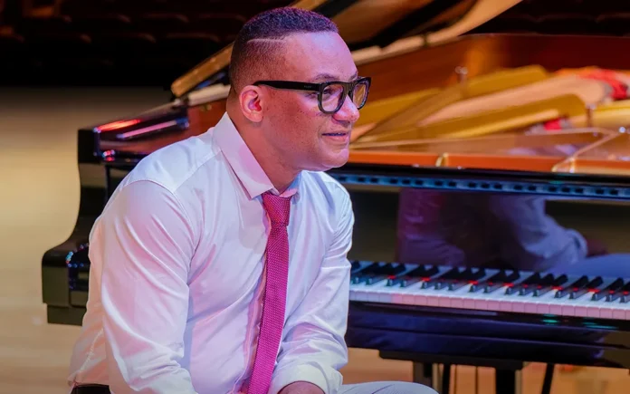Gonzalo Rubalcaba sentado ante un piano de cola en un escenario con iluminación cálida.