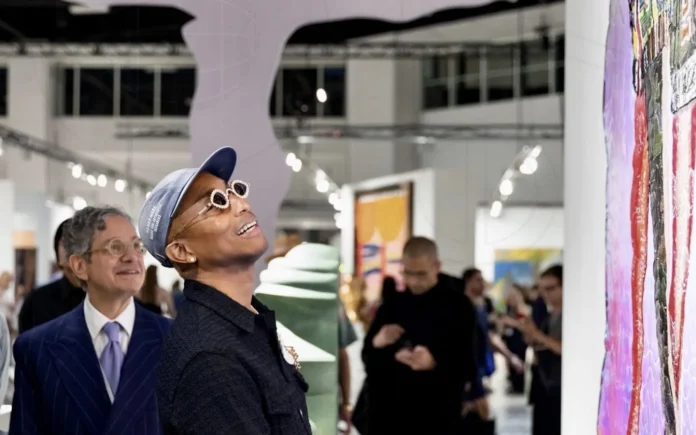 Visitantes observan pinturas y una gran silueta blanca de brazos abiertos en una sala de Art Basel Miami Beach.
